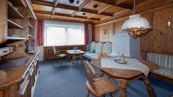 A wooden cabin interior with a dining table, chairs, a sofa, and a window with curtains.