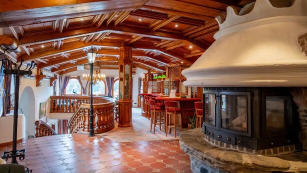 A wooden interior with a stone fireplace, a bar area, and a staircase leading to a balcony.