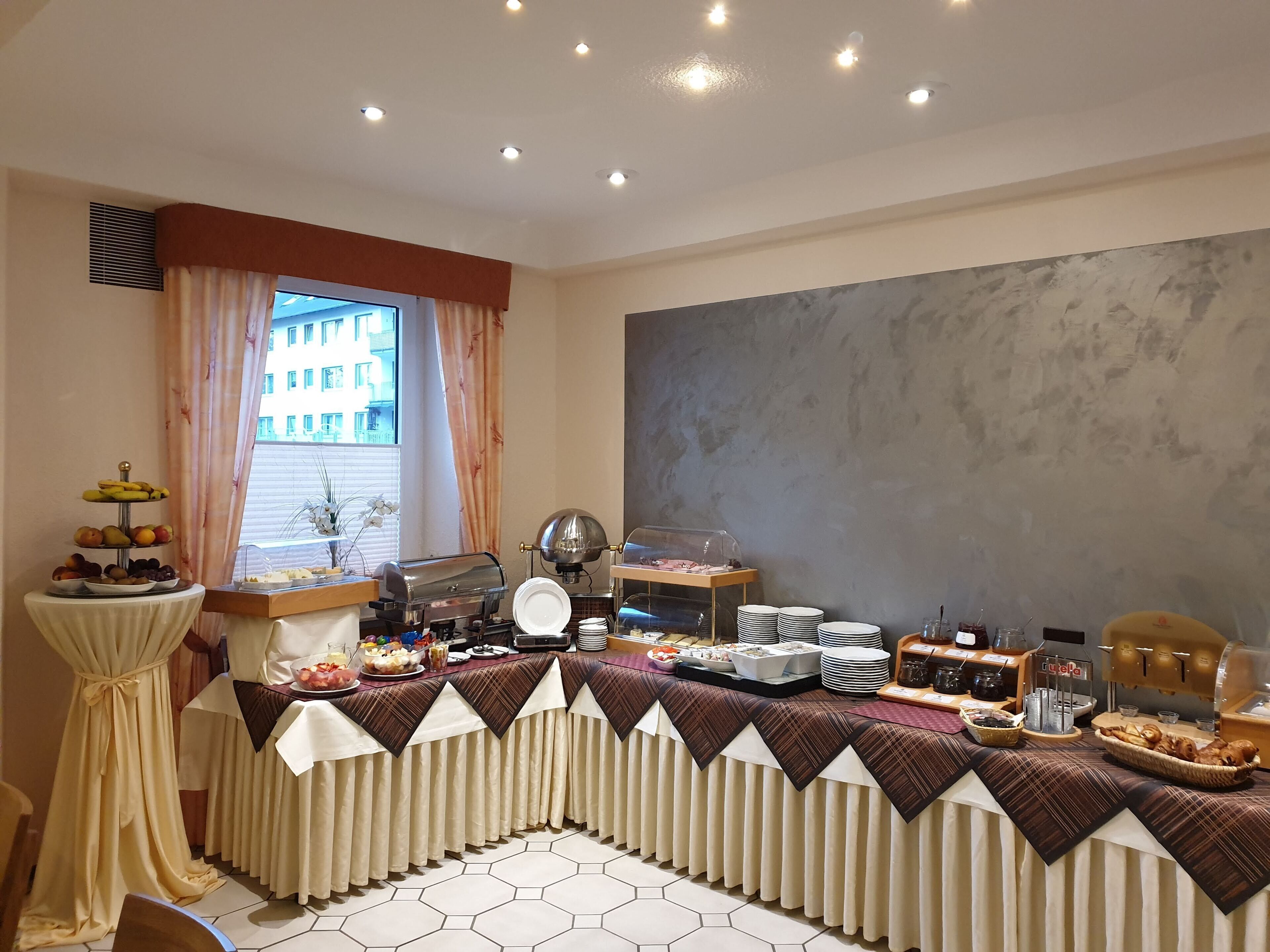 A buffet setup with a variety of food items, a coffee machine, and a window with a view of buildings.