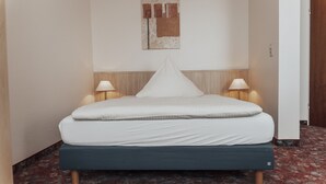 Una cama bien hecha con cabecera de madera, dos lámparas de noche y un cuadro pequeño en la pared.