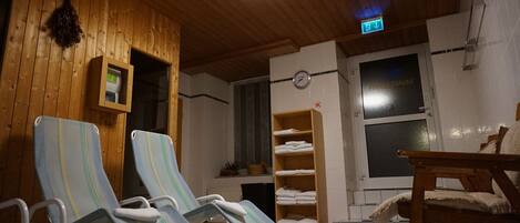 Ett rum med träväggar, en taklampa, en klocka, ett fönster och en hylla med handdukar.