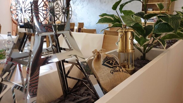 Una mesa con una escultura de metal, un farol, una planta y un saco de arpillera con texto.