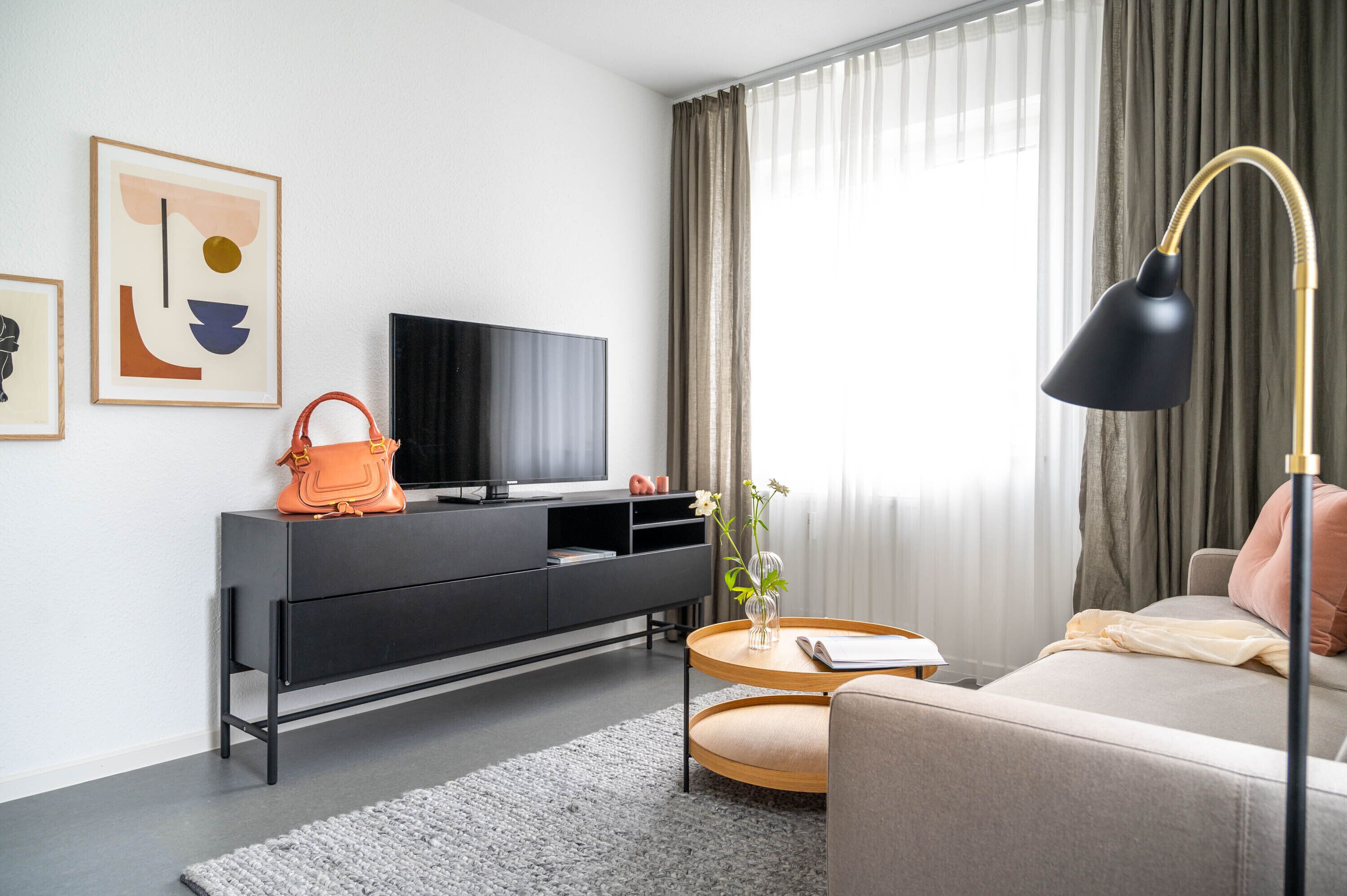 A modern living room with a sofa, a coffee table, a TV on a black cabinet, and a lamp.