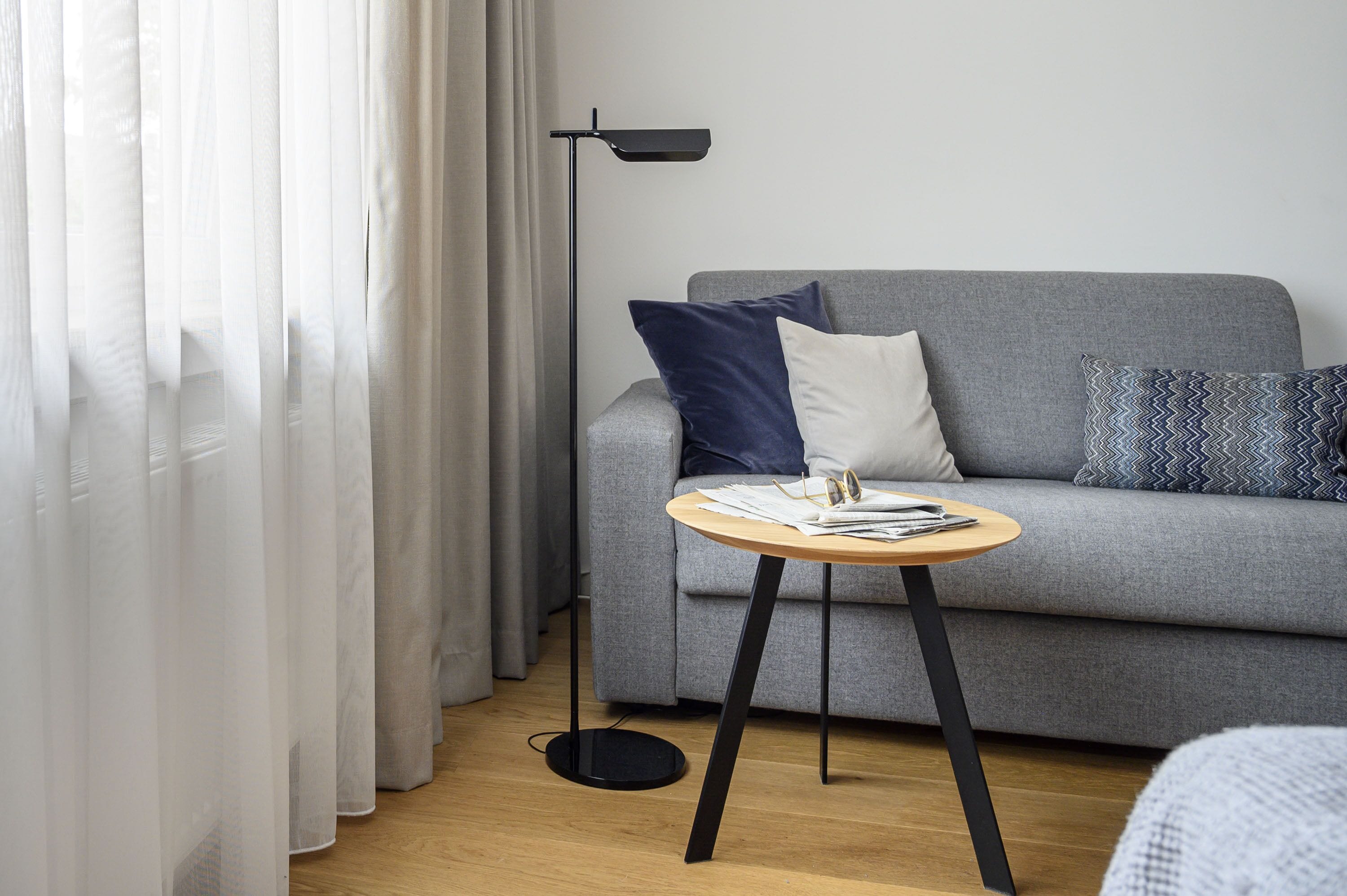 Una sala de estar moderna con un sofá gris, una mesita redonda de madera y una lámpara de pie negra.