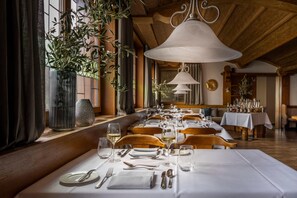 A restaurant with a long dining table set for a meal, wooden chairs, and hanging plants.