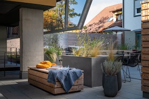 An outdoor seating area with a wooden bench, a potted plant, and a table with chairs.