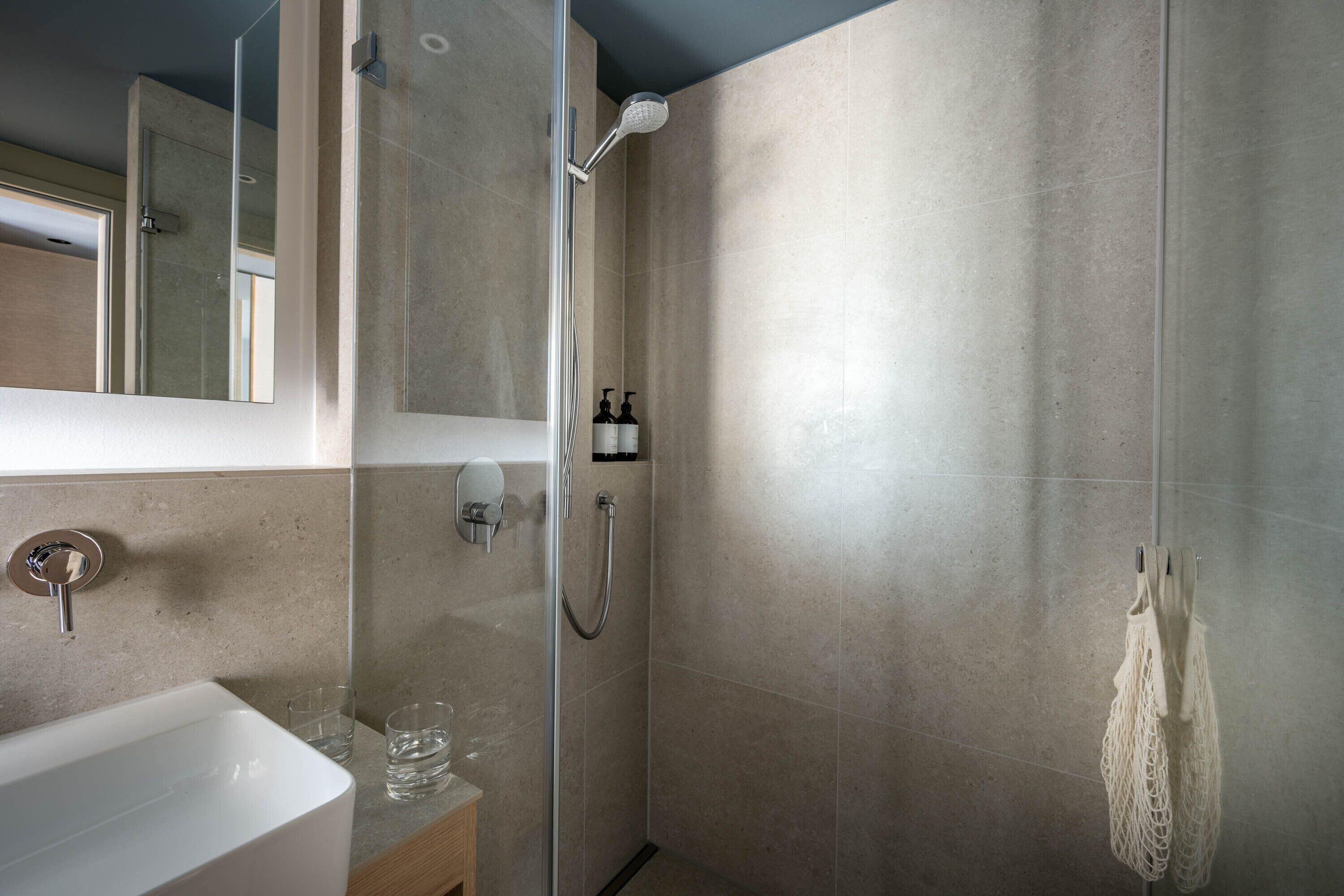 A modern bathroom with a glass-enclosed shower, a white sink, and a mirror.