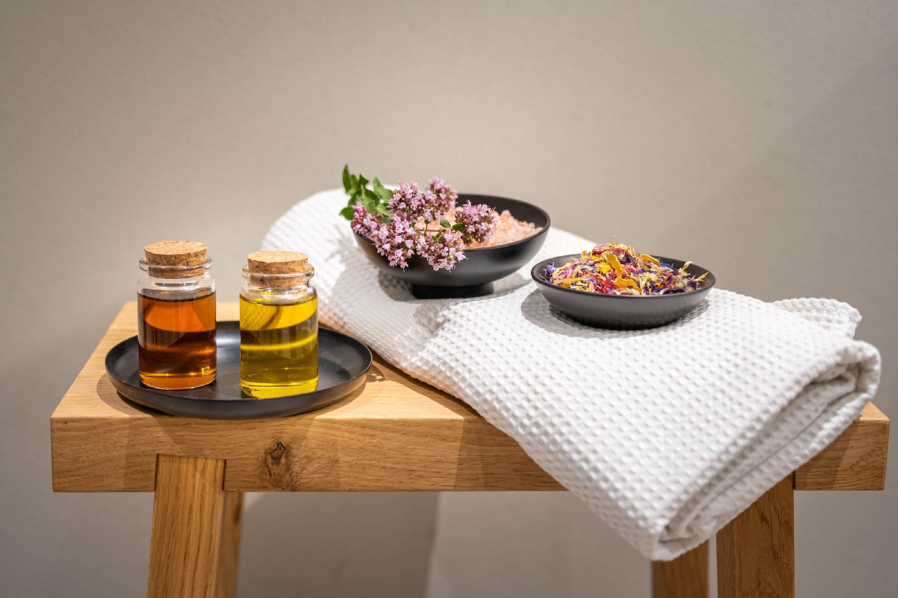 Une table en bois sur laquelle reposent deux petits flacons en verre, un bol rempli de fleurs roses et un autre bol contenant un assortiment de fleurs séchées aux couleurs vives.