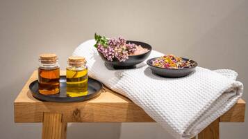 A wooden table with two small glass bottles, a bowl of pink flowers, and a bowl of colorful dried flowers.