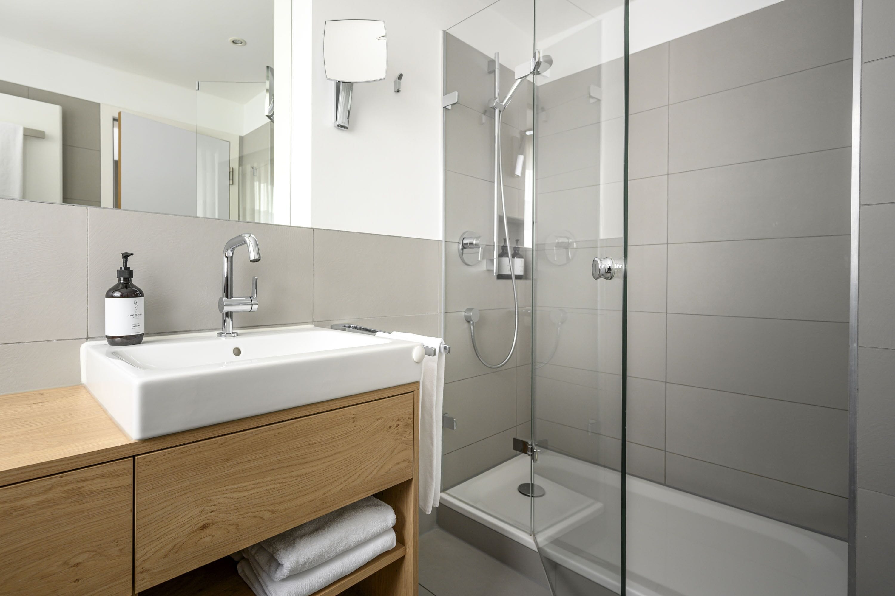 A modern bathroom with a white sink, wooden vanity, a glass shower enclosure, and a mirror.
