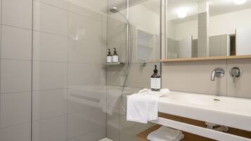 Un baño moderno con ducha de vidrio, un lavabo blanco y un espejo encima.