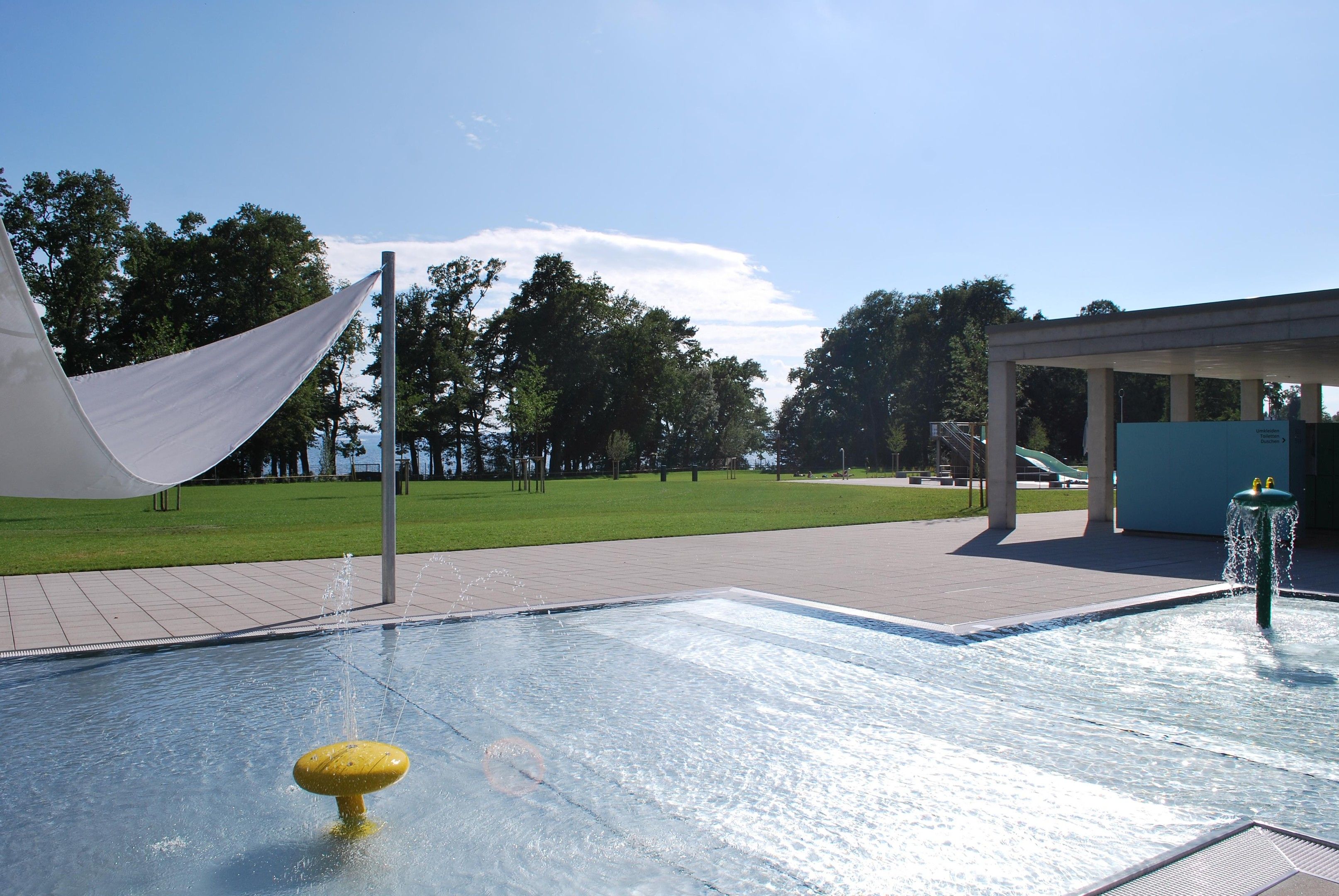 En swimmingpool med en fontän, ett avskärmat sittområde och en gräsyta i bakgrunden.