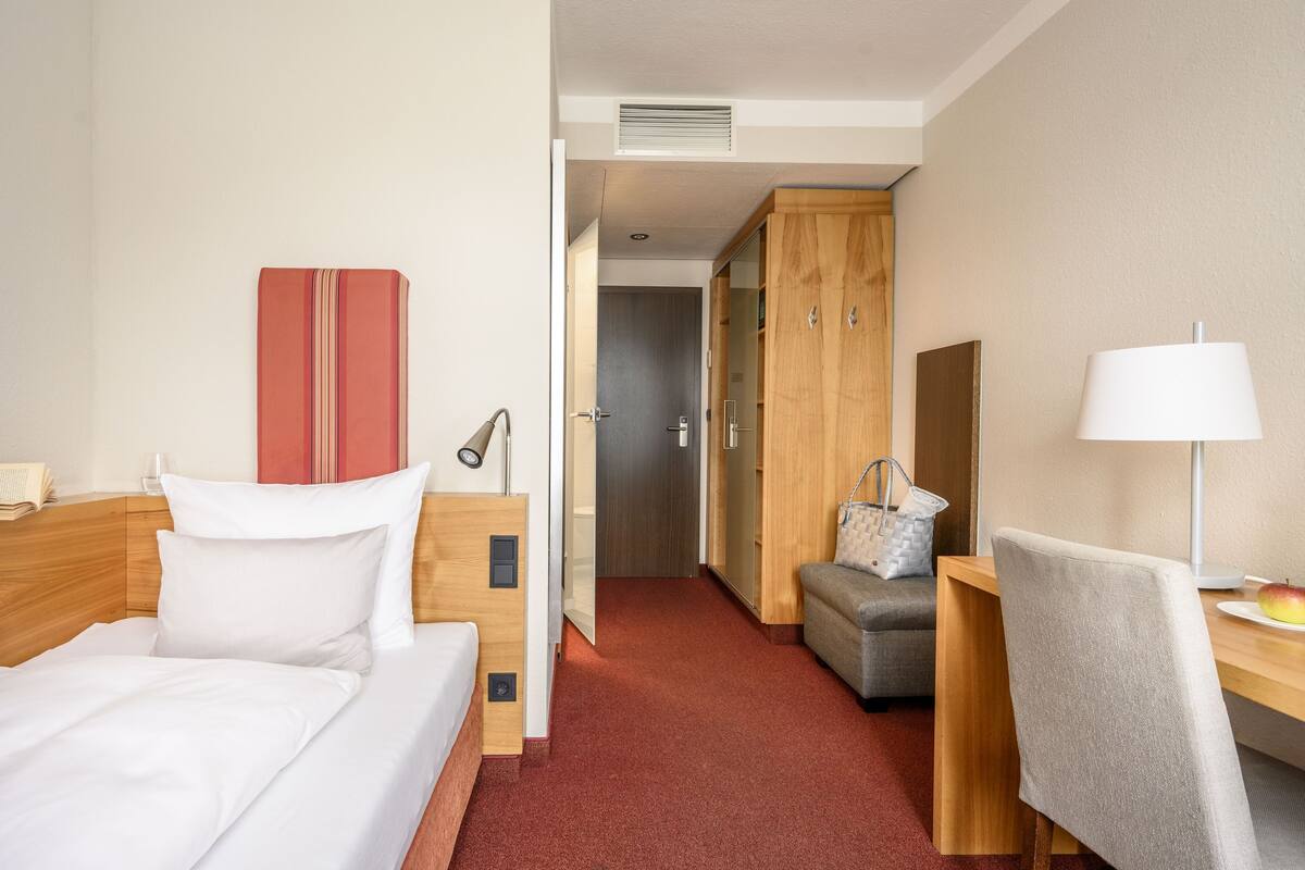 A hotel room with a bed, a desk, a chair, a lamp, and a wardrobe.
