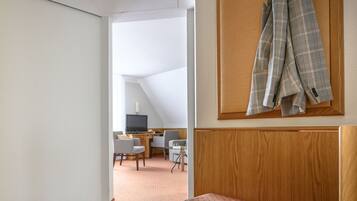 Ein Hotelzimmer mit einer Holzbänkl, einem Schreibtisch mit Stühlen und einem Fernseher.