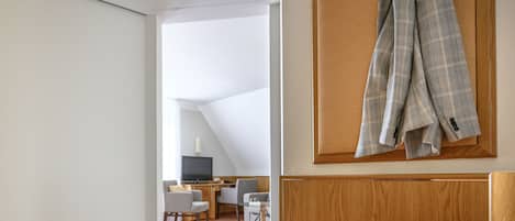 Quarto de hotel com um banco de madeira, uma escrivaninha com cadeiras e uma televisão.