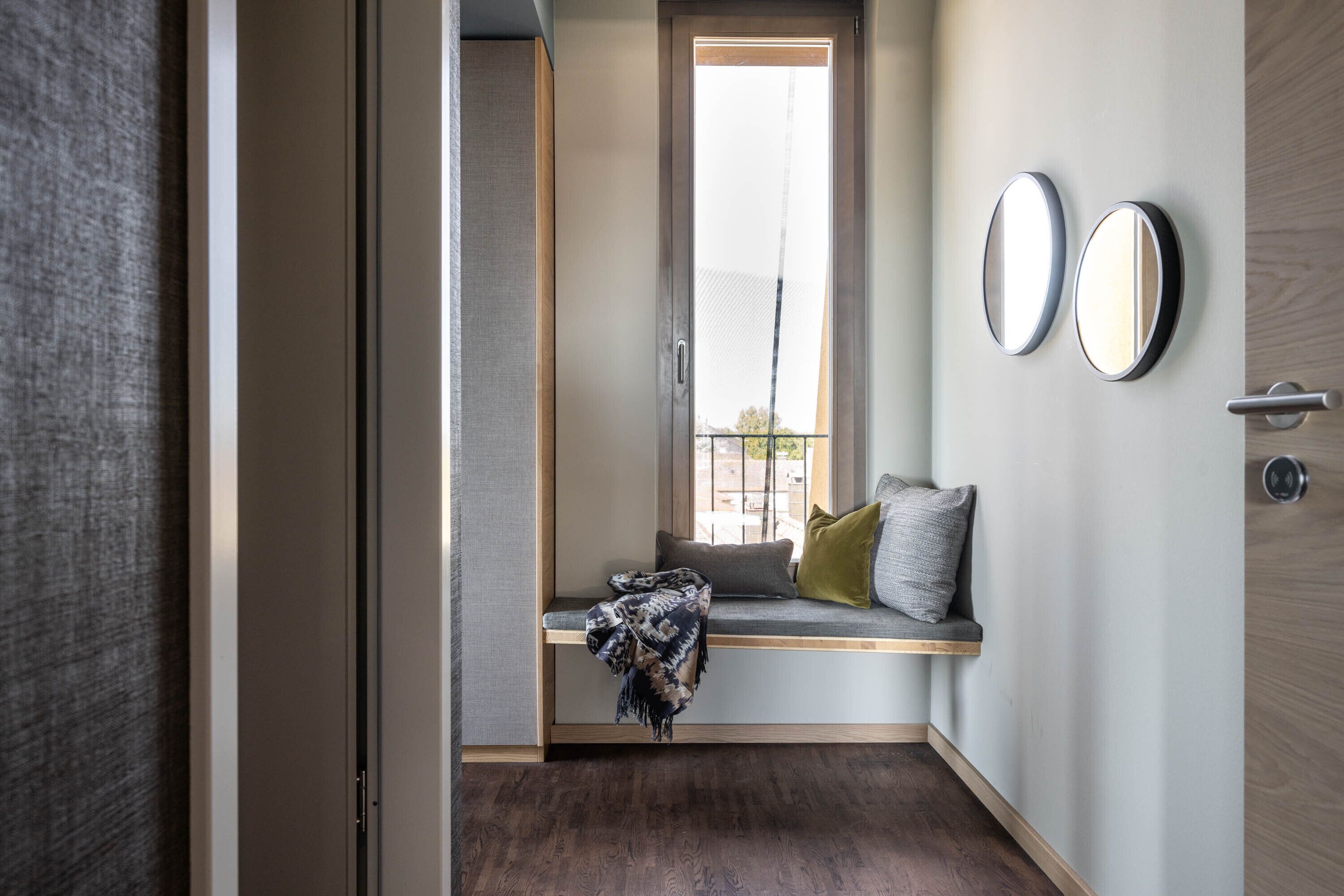 Un interno moderno con una panca integrata, una finestra vista e due specchi fissati alla parete.