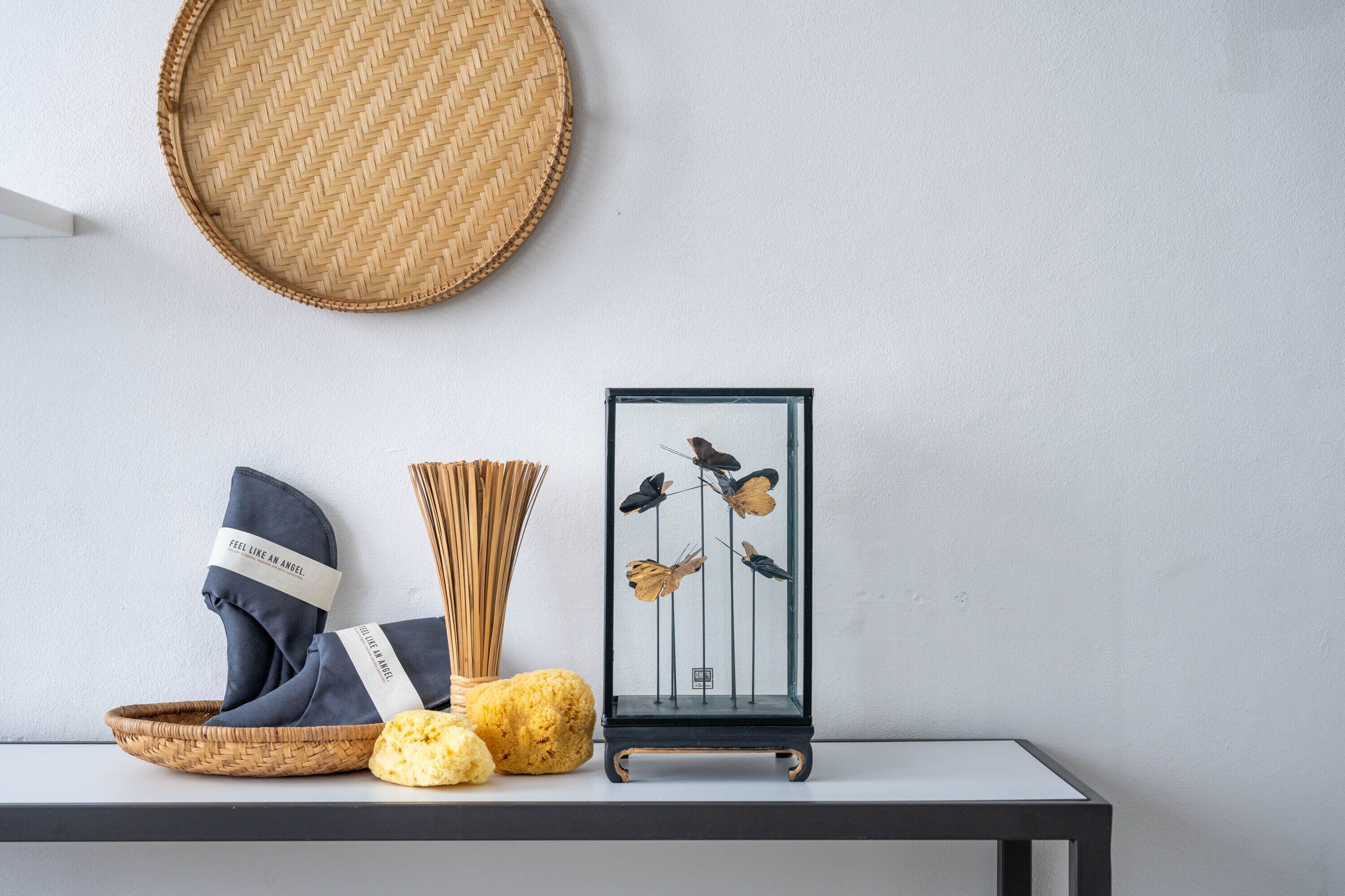 Een plank met een geweven mand, een glazen vitrine met gedroogde bloemen en een rond geweven vloermat.