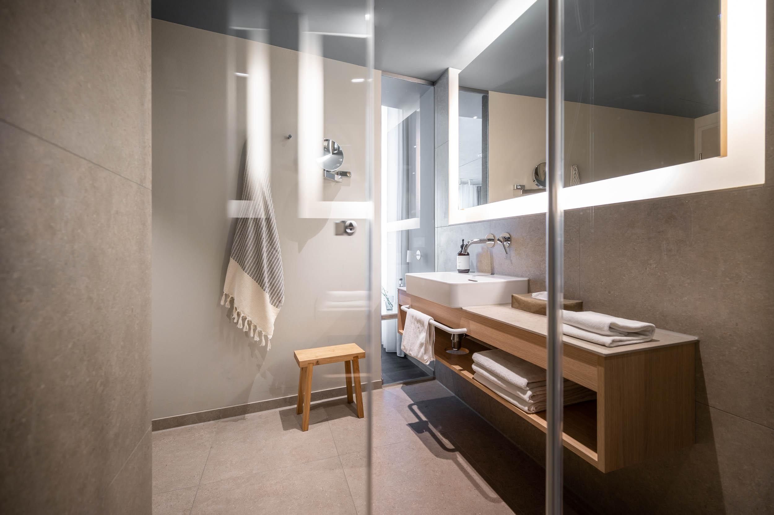Un baño moderno con cabina de ducha de vidrio, tocador de madera y un espejo grande.
