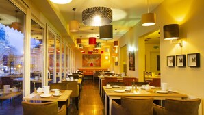 A restaurant with multiple dining tables and chairs, large windows, and hanging pendant lights. - Hotel Bad Emser Hof (Bad Ems)
