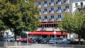 A hotel with multiple balconies, a stone wall, and parked cars along a river. - Hotel Bad Emser Hof (Bad Ems)