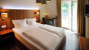 A hotel room with a large bed, wooden headboard, bedside lamps, a desk with a chair, and a television. - Hotel Bad Emser Hof (Bad Ems)
