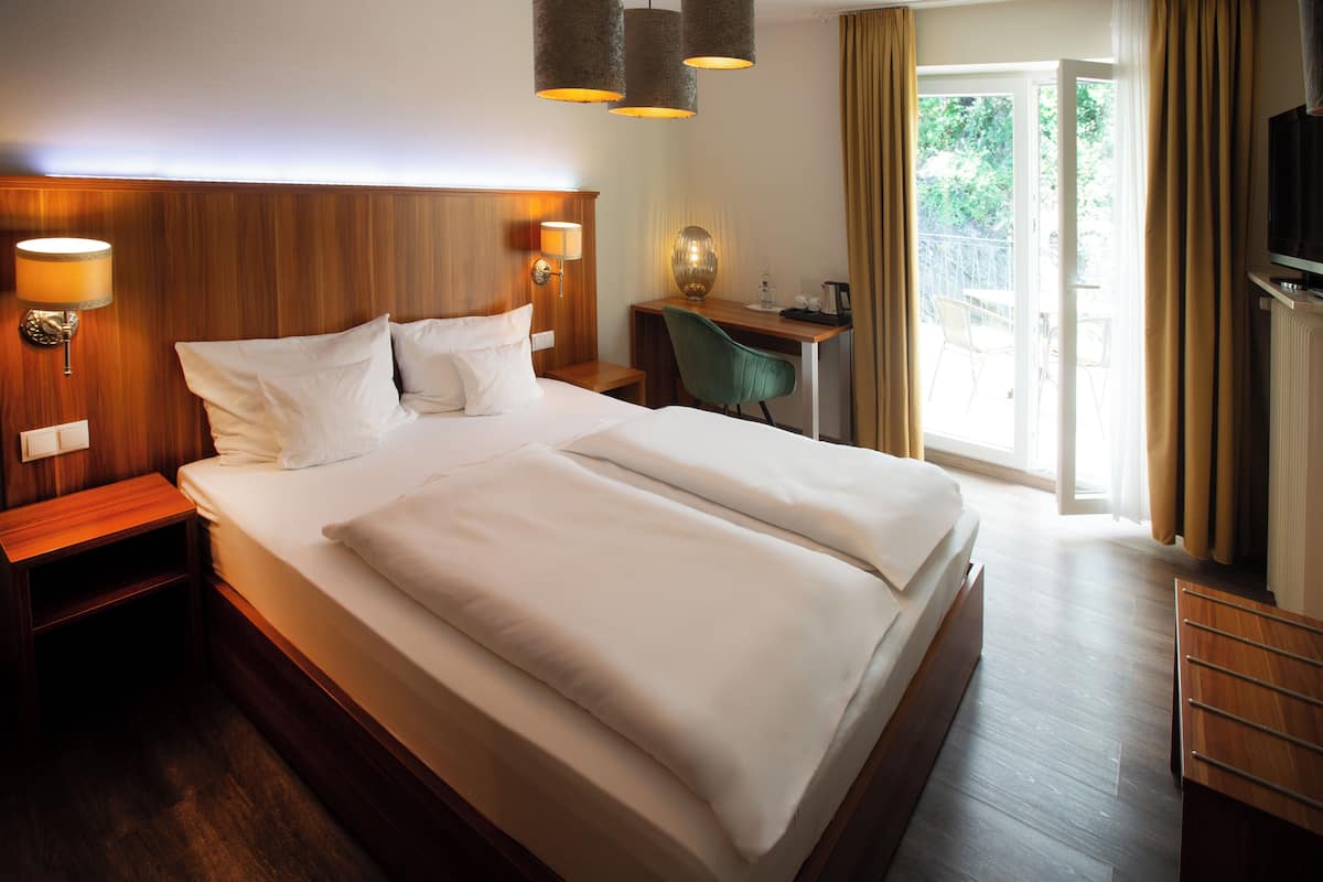 A hotel room with a large bed, wooden headboard, bedside lamps, a desk with a chair, and a television.
