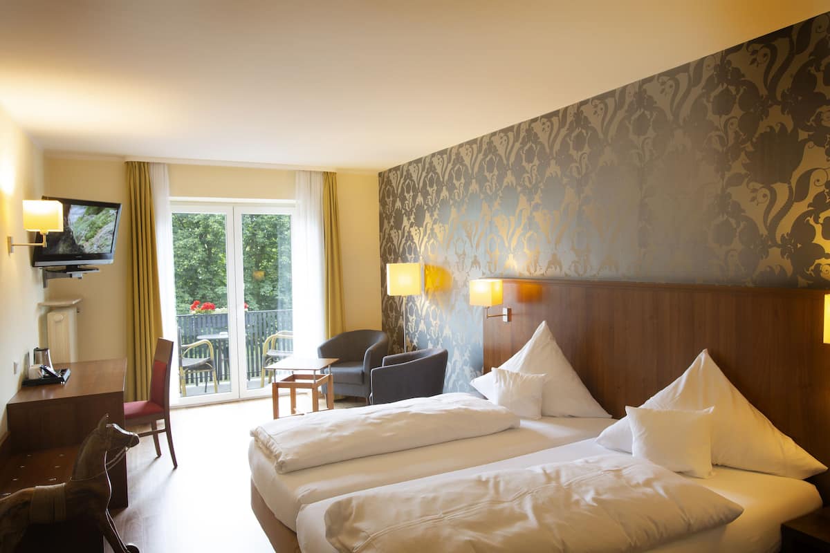 A hotel room with two beds, a desk, a chair, and a TV.