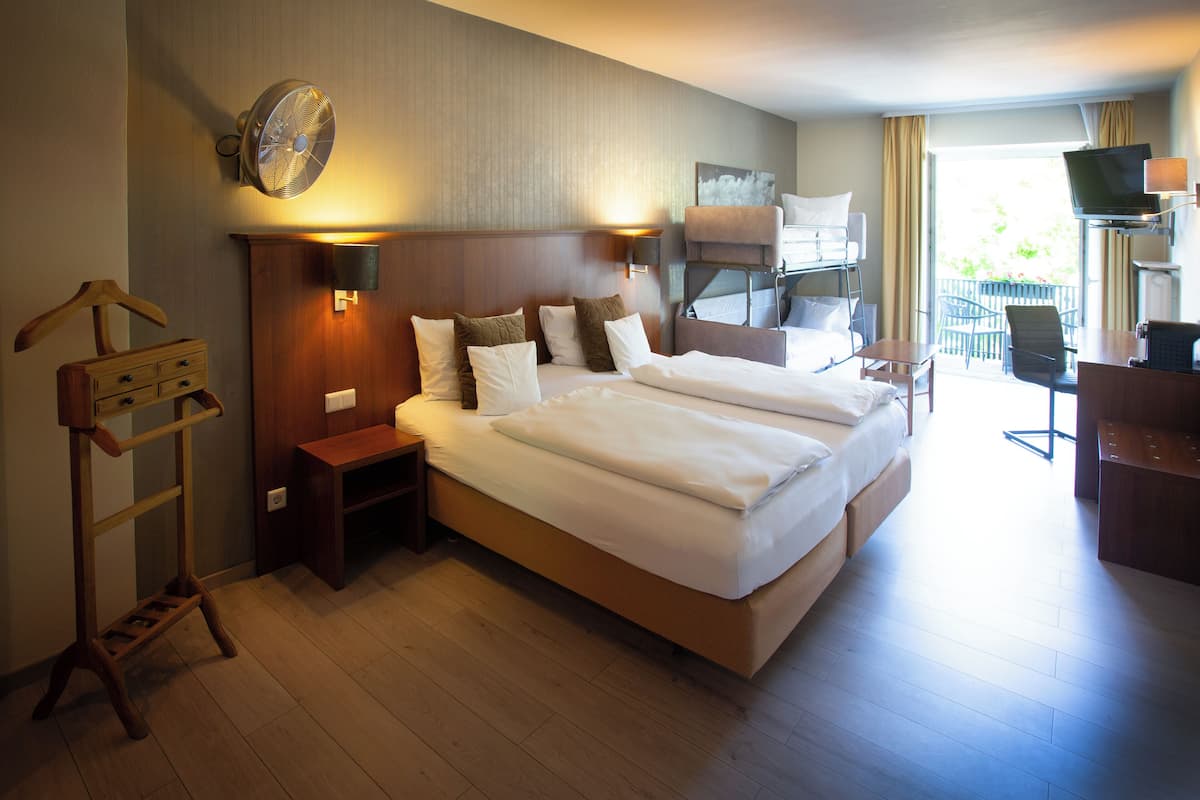 A hotel room with a large bed, bedside tables, a desk, a chair, a TV, and a balcony with a view.