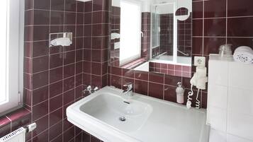 Une salle de bain avec un lavabo blanc, un miroir et une cabine de douche en verre.