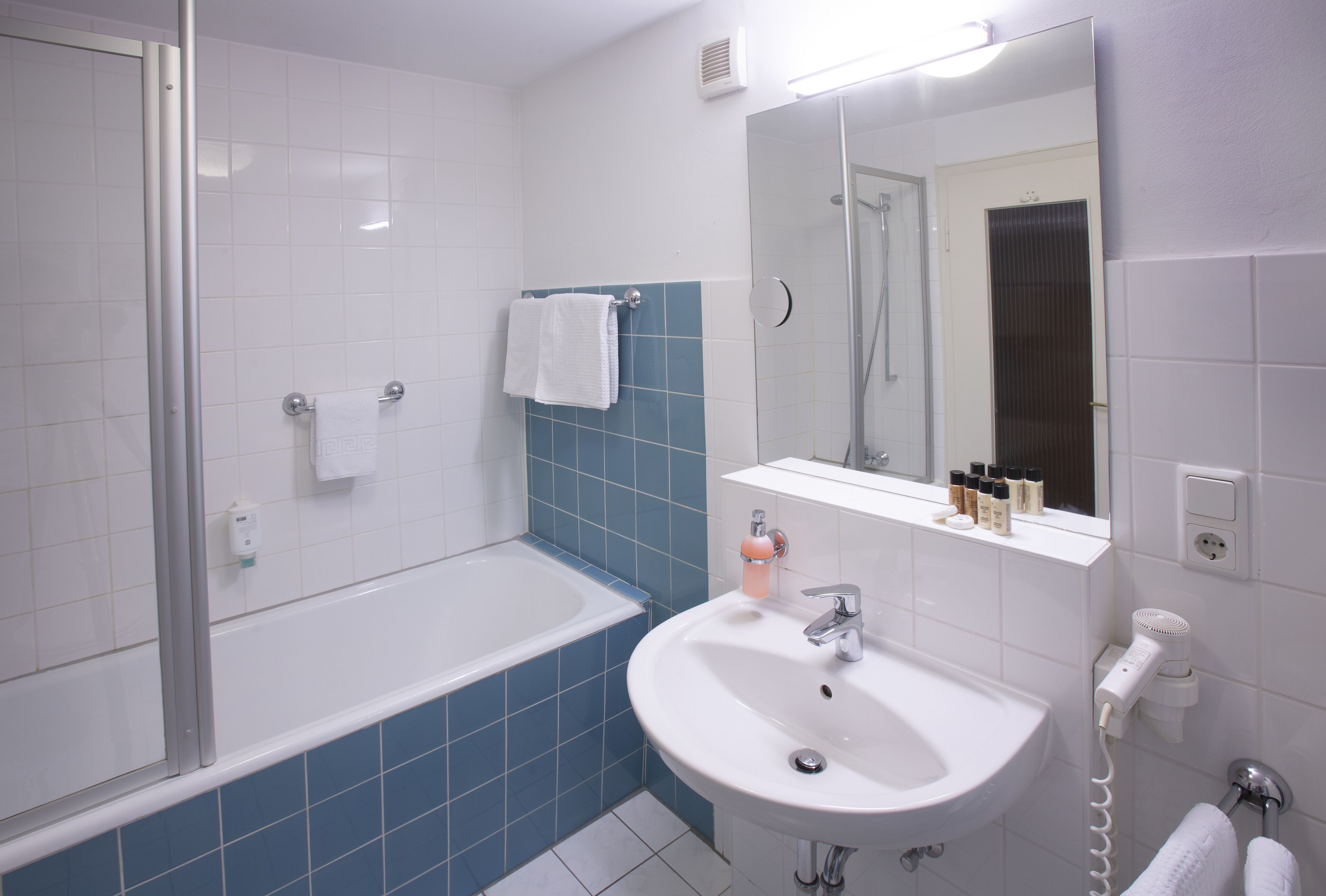 Een badkamer met een bad, een wastafel, een spiegel en een handdoekhouder.