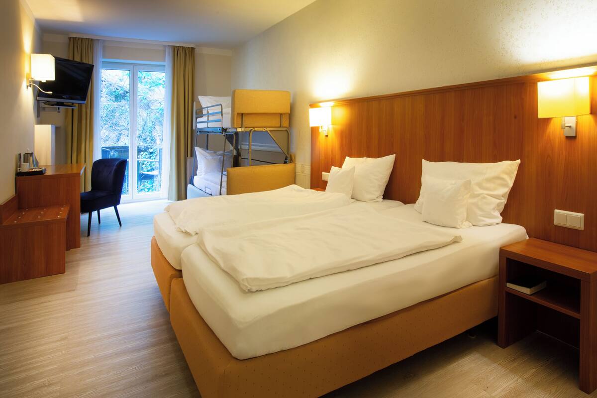A hotel room with a large bed, a desk, a chair, a television, and a window with curtains.