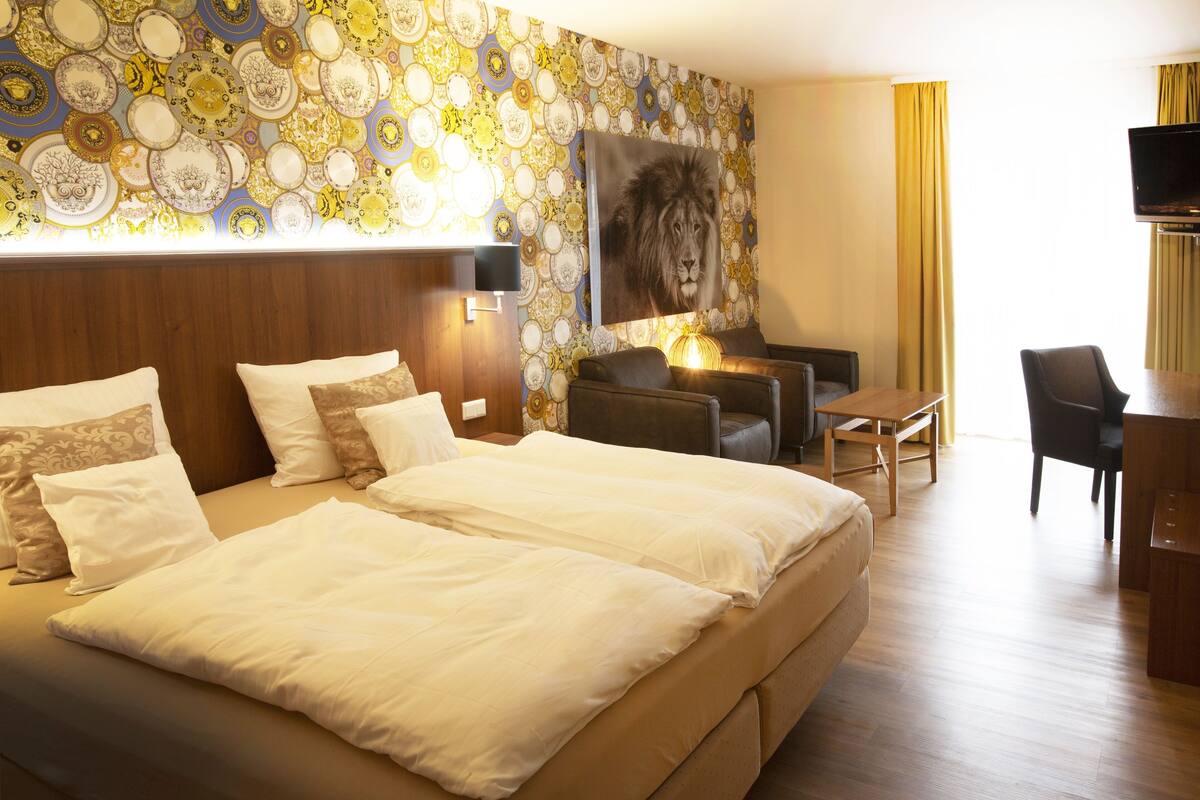 A hotel room with a large bed, a desk, a chair, a television, and a wall decorated with plates.