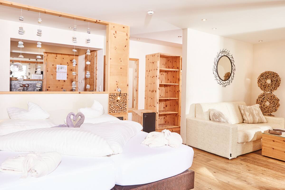 Habitación de hotel con cama, sofá, armario de madera, espejo y una pared decorada.