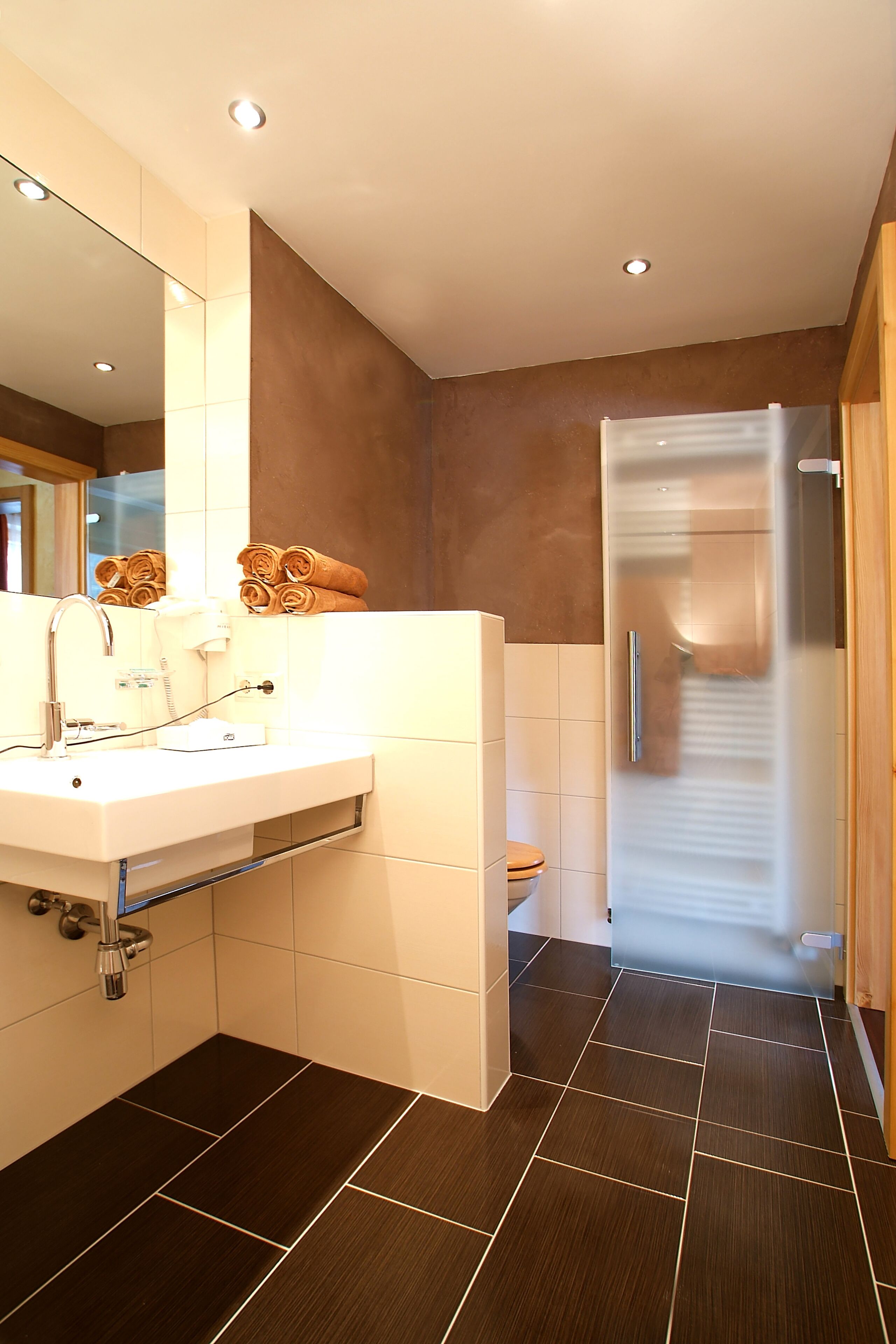 A modern bathroom with a white sink, mirror, and towel rack. There is a toilet and a glass shower enclosure.