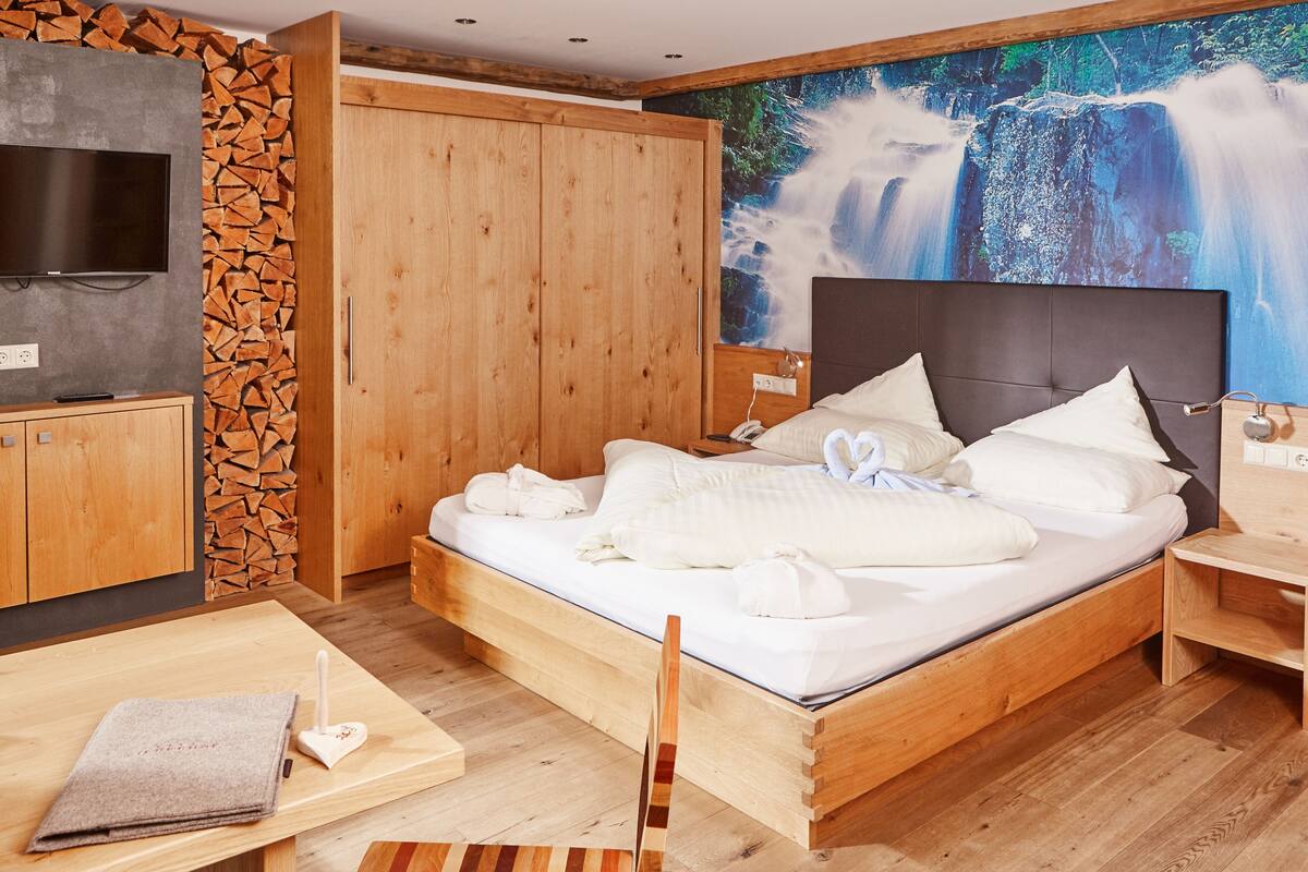 Un dormitorio con cama de madera, televisor, armario de madera y un amplio mural de cascada en la pared.