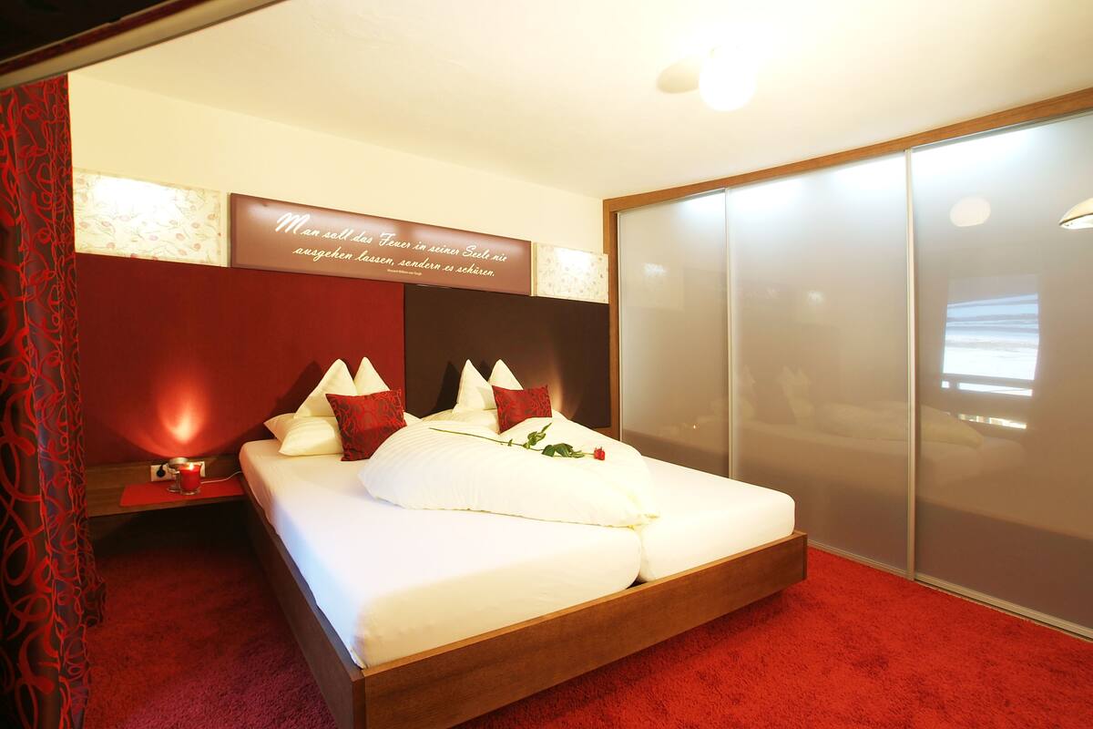 Una habitación de hotel con una cama grande, una mesita de noche con lámpara, alfombra roja y un armario con puerta corredera.