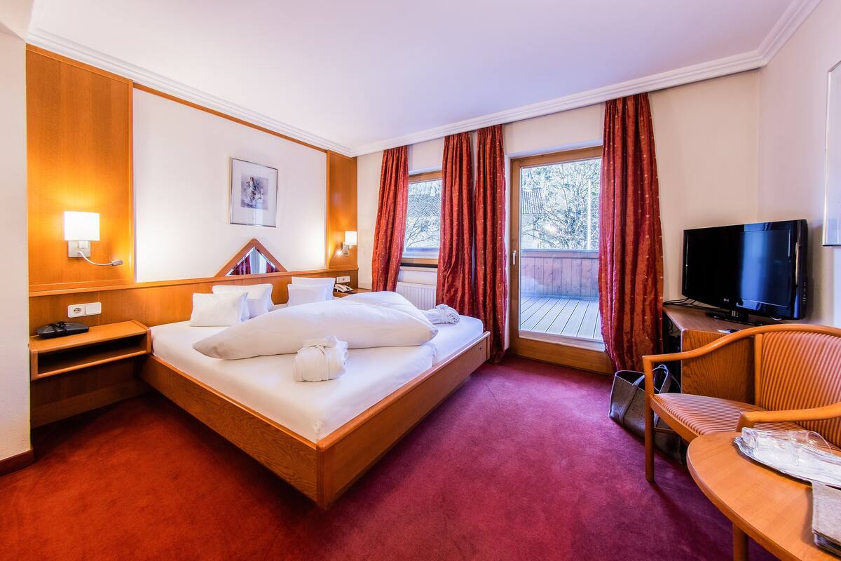 Una habitación de hotel con una cama grande, televisión, escritorio y ventana con cortinas.