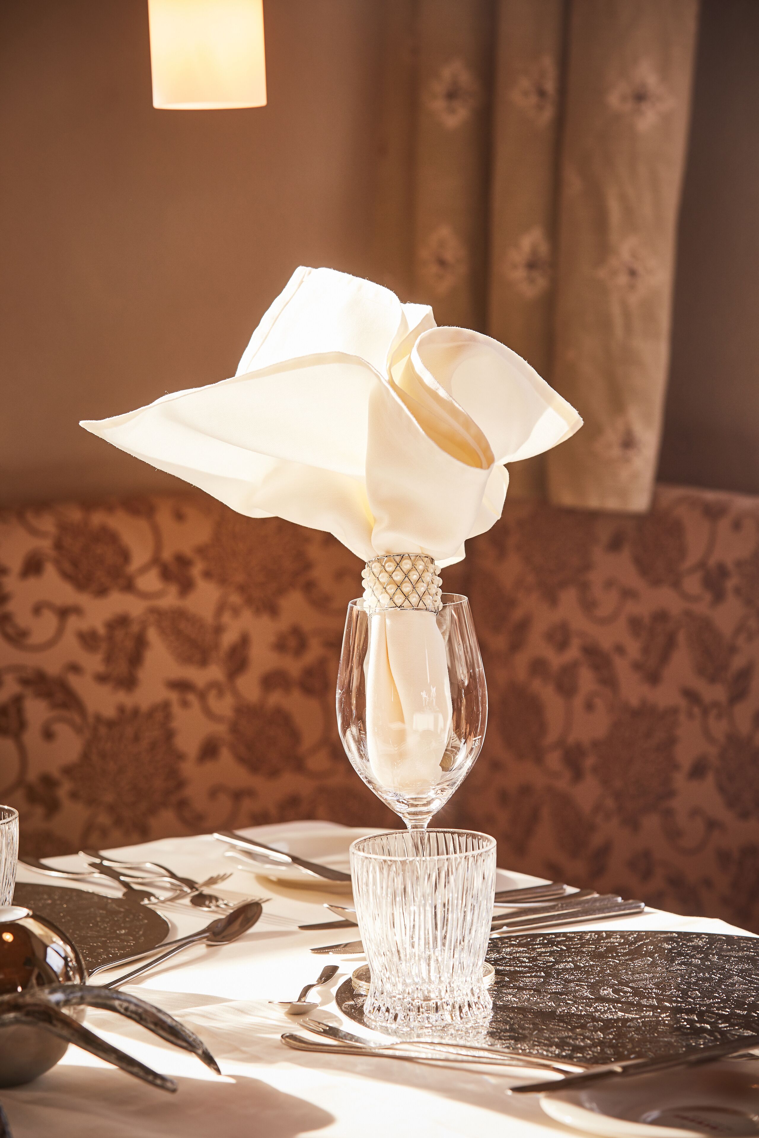 A table set for a meal with a white flower arrangement in a glass vase, a clear glass, and a patterned table runner.