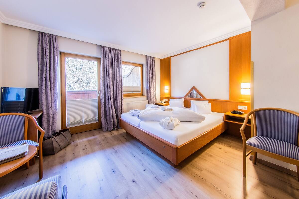 Habitación de hotel con cama, dos sillas, televisión y ventana con cortinas.