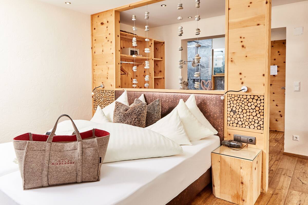 Habitación de hotel con cama, cabecera de madera, mesita de noche con lámpara y un espejo grande.