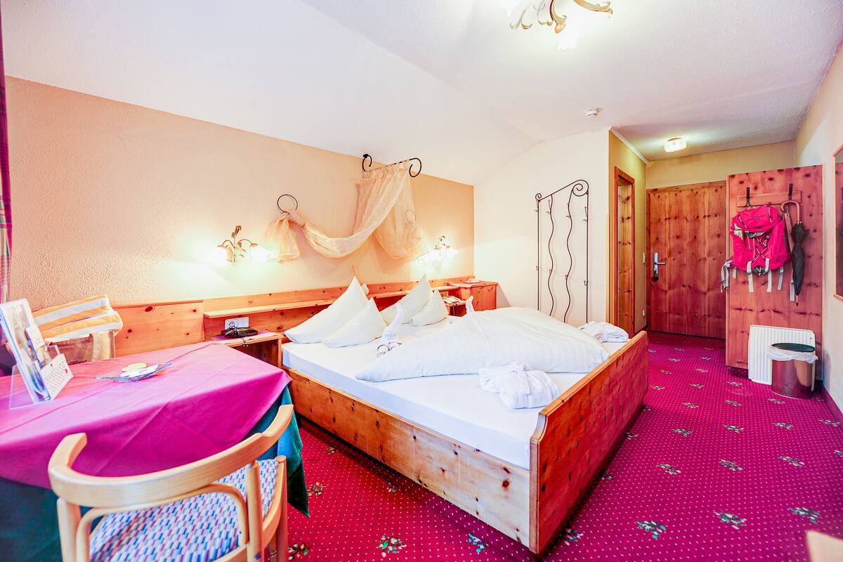 Un dormitorio con una cama de madera, una mesita con mantel rosa y una silla.