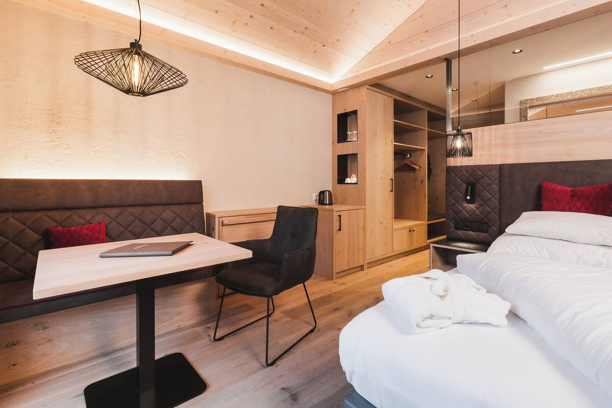 Una habitación de hotel moderna con una cama, un escritorio con una computadora portátil, una silla, un armario y una lámpara colgante.