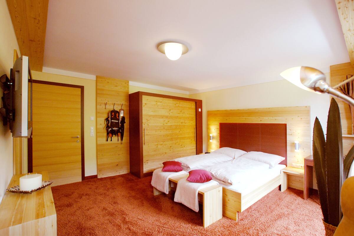 Un dormitorio con cabecera de madera, cama con ropa blanca, mesita de noche, lámpara y televisor montado en la pared.