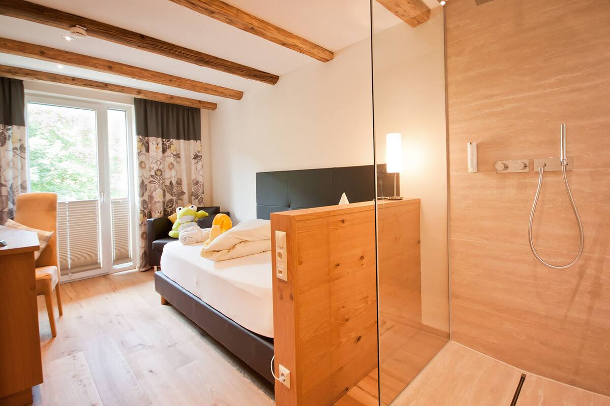 Un dormitorio moderno con cabecera de madera, cama con almohadas, un escritorio y un separador de vidrio.