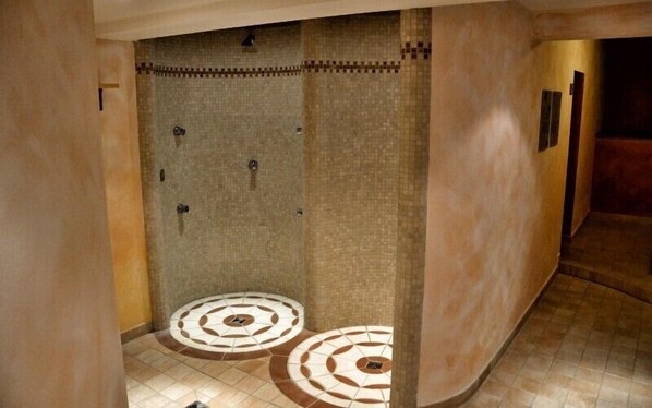 A shower area with a tiled wall and floor, a towel rack, and a circular design on the floor.