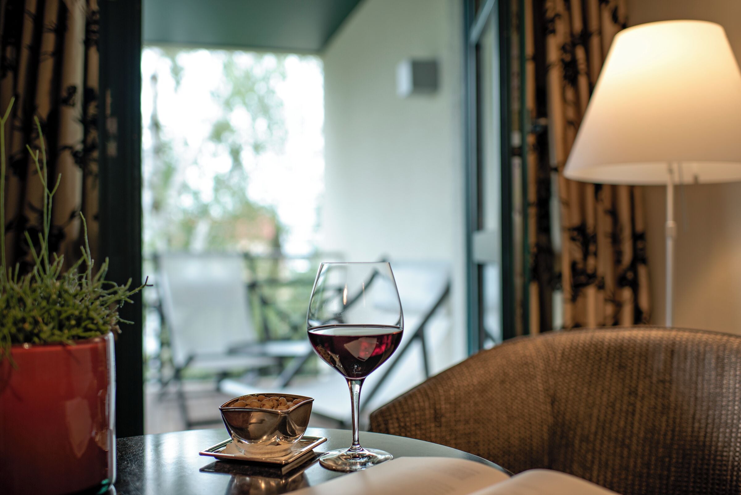 A table with a glass of red wine, a bowl, and a potted plant.