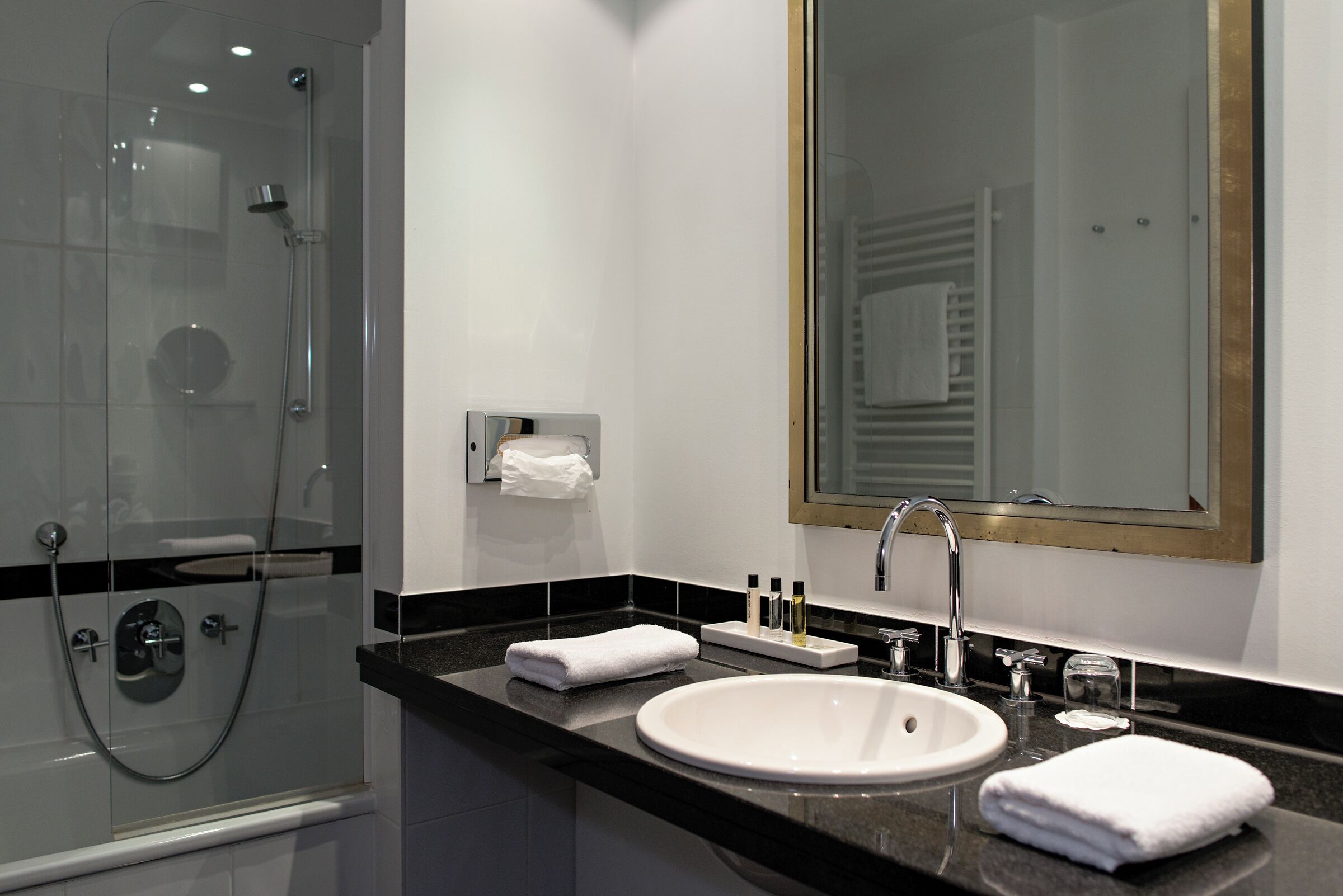 A modern bathroom with a glass-enclosed shower, a white sink, and a large mirror.