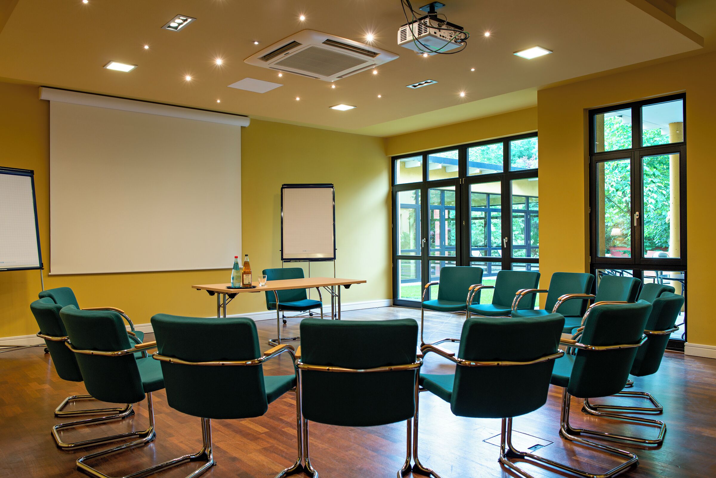 Ein Konferenzraum mit Projektor, Whiteboard und grünen Stühlen.