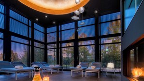 A modern spa area with large windows, lounge chairs, a fireplace, and a table with candles. - Zeller Hotel & Restaurant (Kahl)