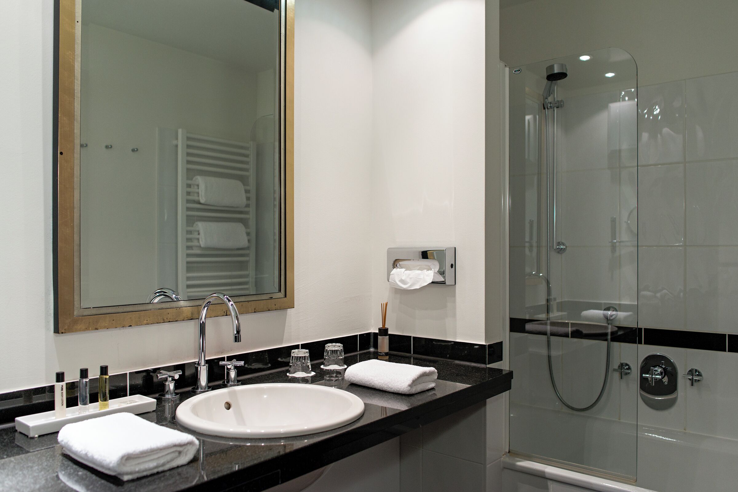 Un baño moderno con un lavabo blanco, un espejo grande y una cabina de ducha con paredes de vidrio.